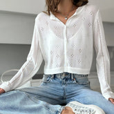 Person wearing a white blouse with eyelet details and blue jeans indoors.